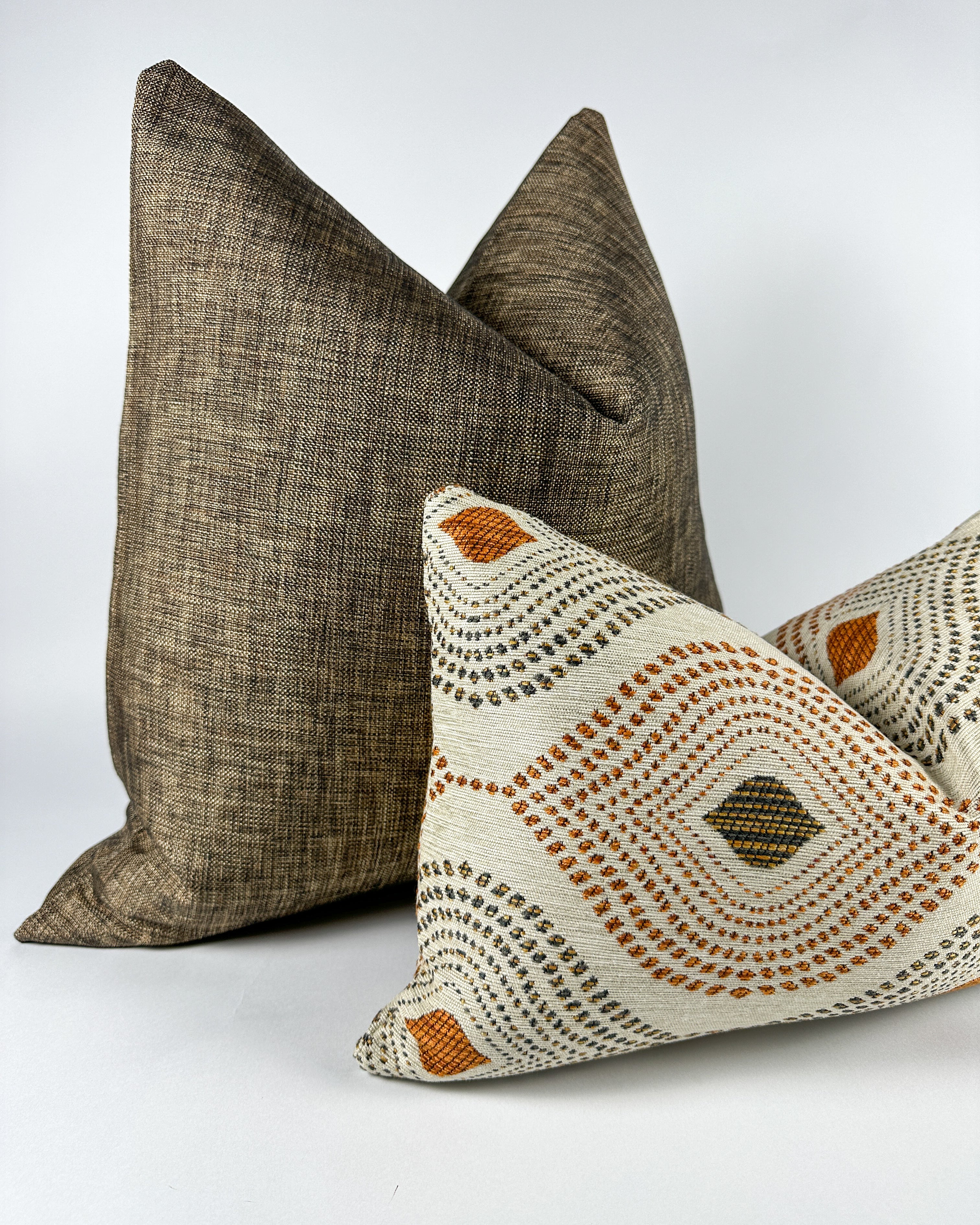 Black textured pillow with ivory, brown and auburn colored lumbar pillow on white backdrop