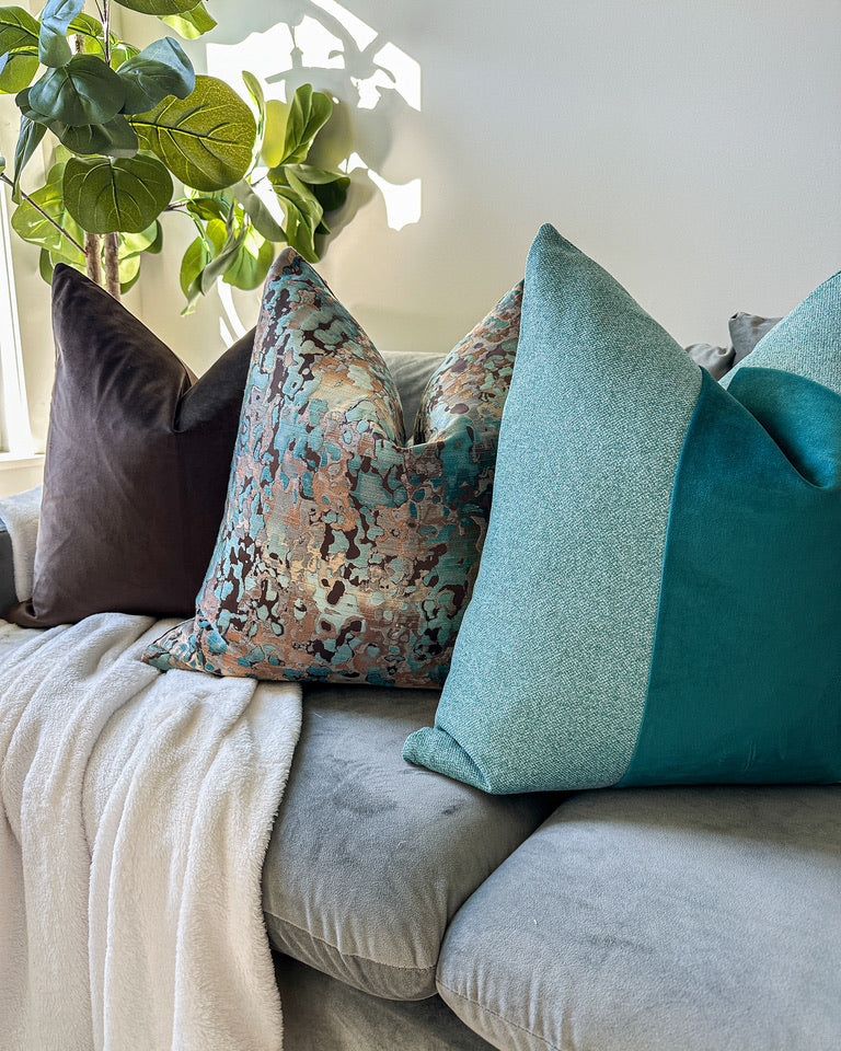 3 pillows staged on a grey couch faux tree in background