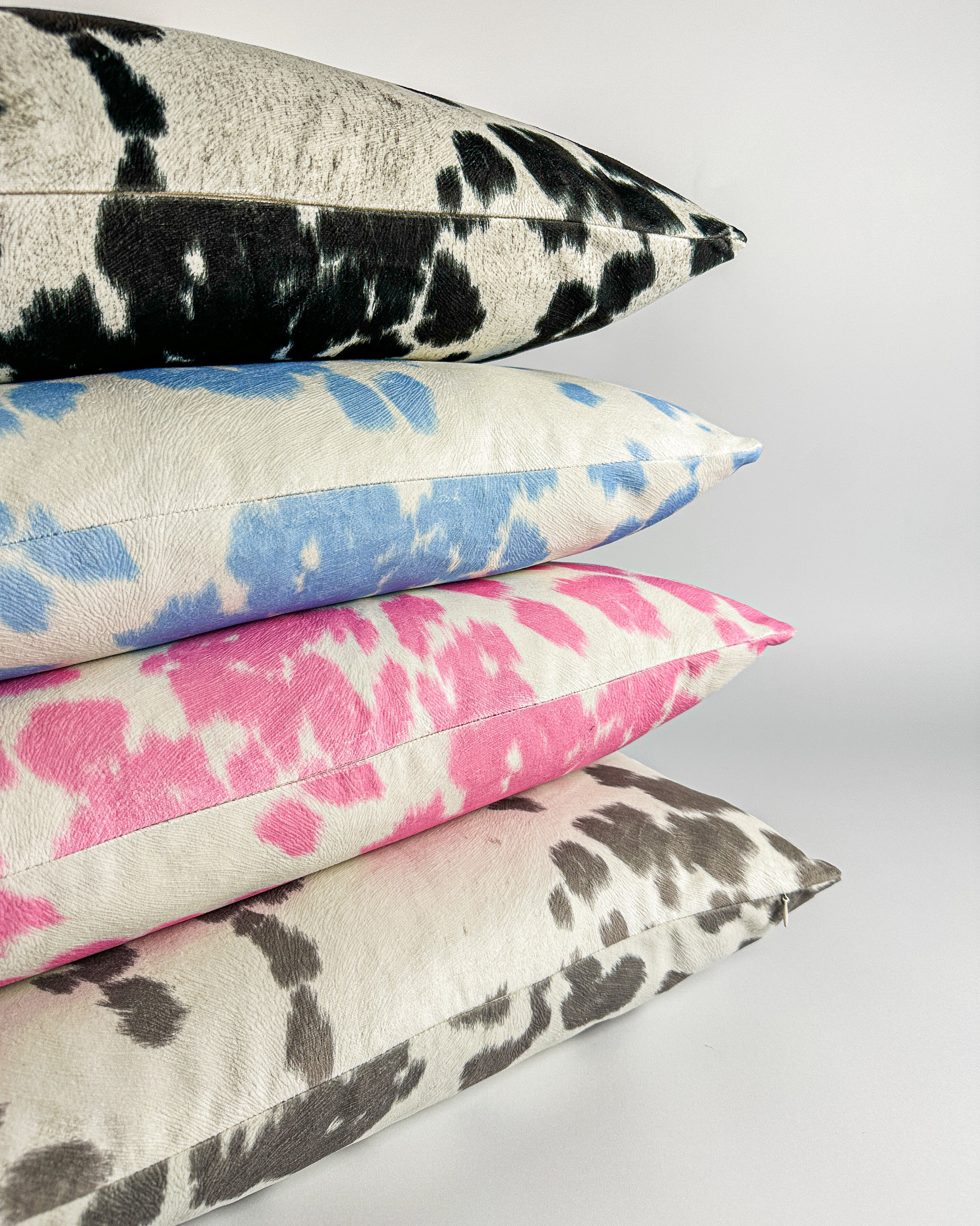 Faux cowhide pillow covers in black, blue, pink and gray colors. Stacked on a white backdrop