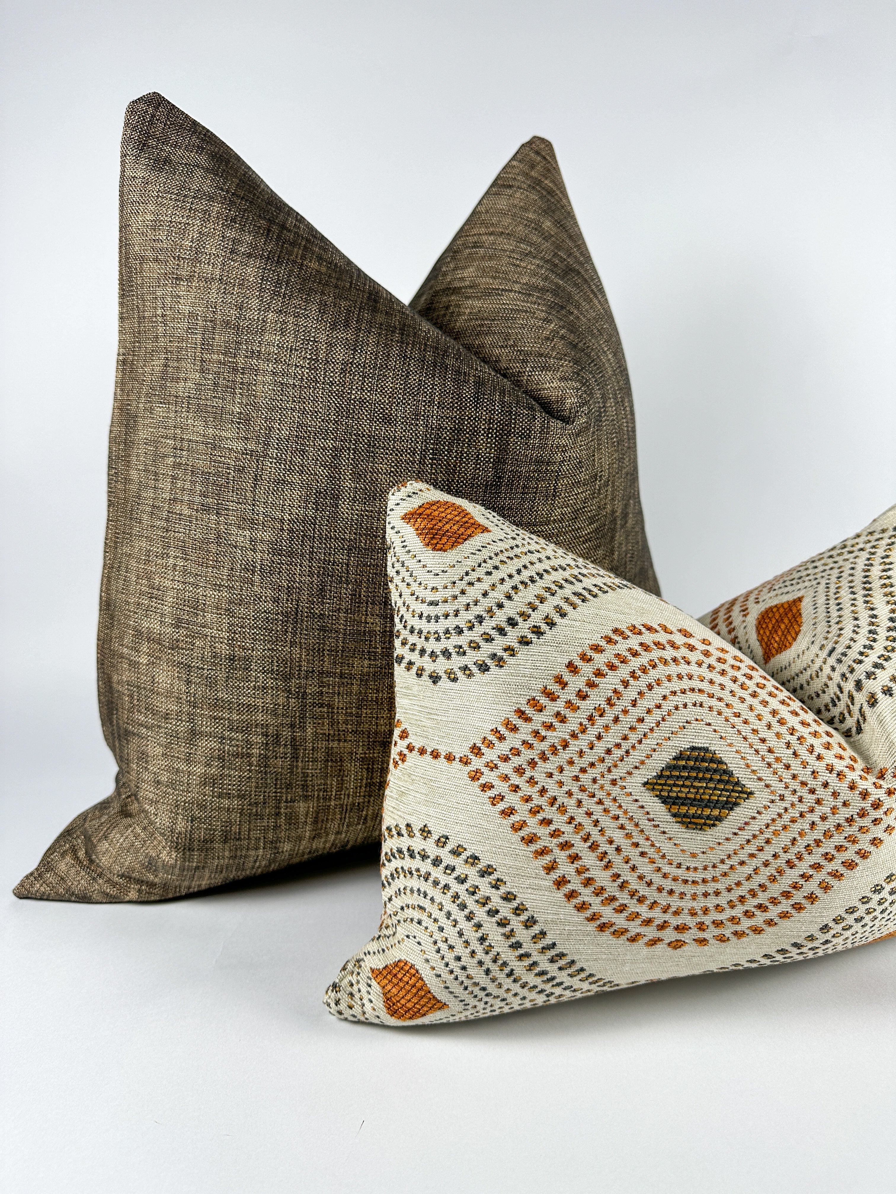 Black textured pillow with ivory, brown and auburn colored lumbar pillow on white backdrop 