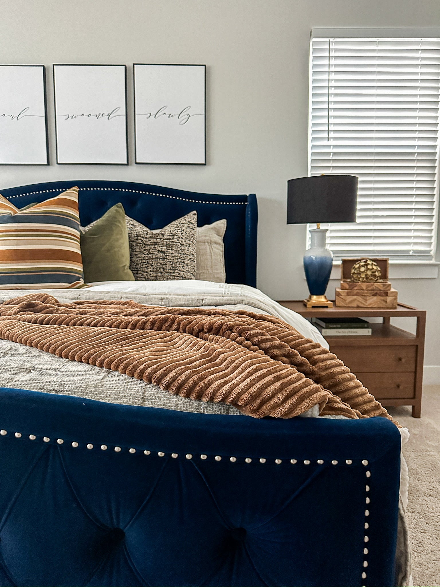 Navy blue bed frame with decorative pillows, lamp and subtle framed wall art