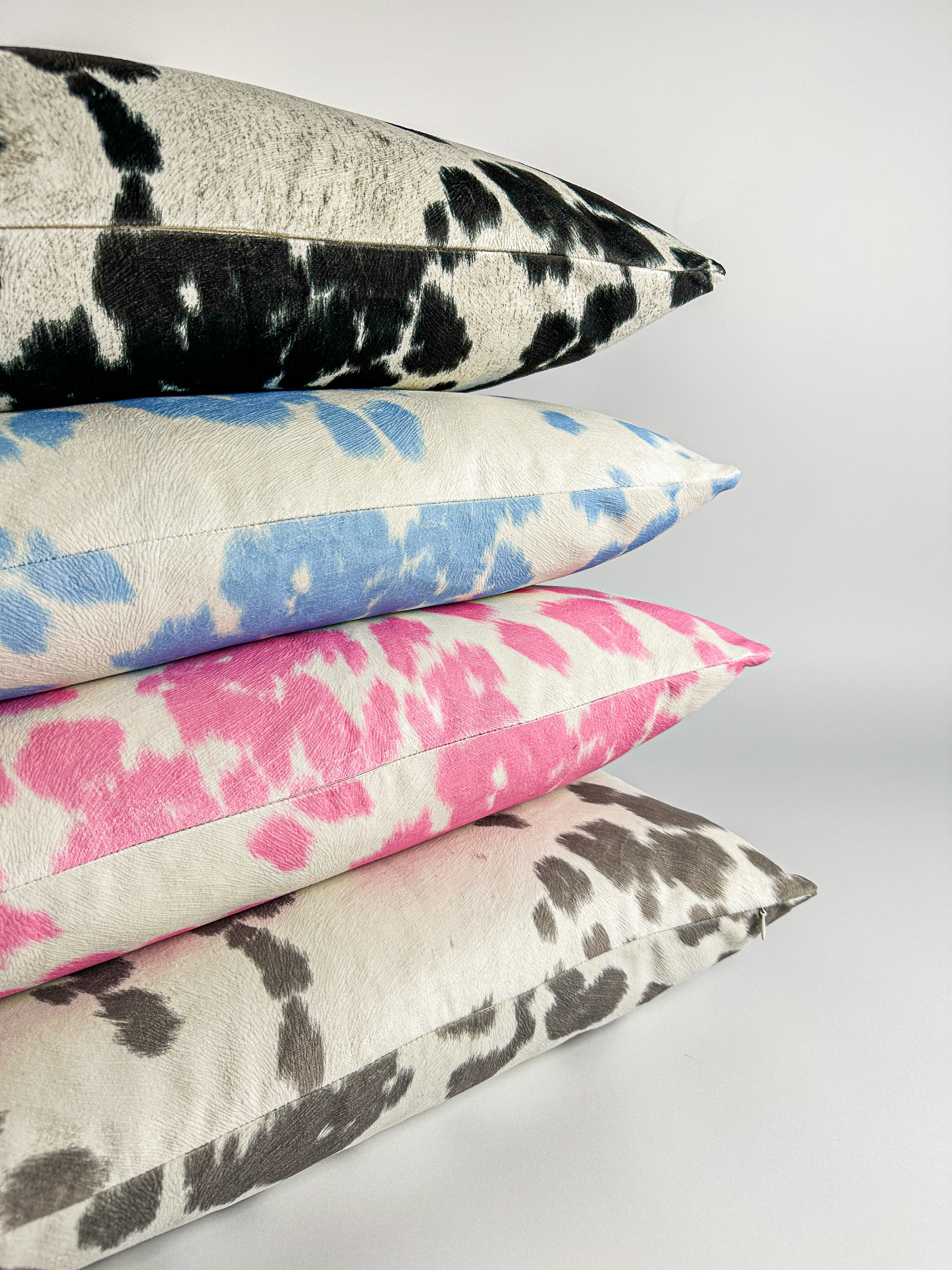 Faux cowhide pillow covers in black, blue, pink and gray colors. Stacked on a white backdrop 